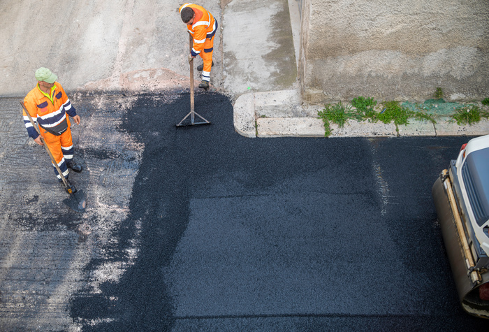 worker leveling fresh asphalt during asphalt pavement repair or construction works