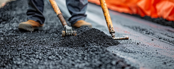 A worker uses a rake to spread asphalt on a road during a road asphalt repair project