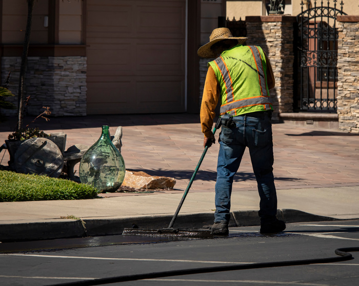 Worker using a sealcoating brush during asphalt parking lot repair